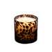 A lit candle in a cylindrical glass holder with a dark brown and amber leopard print pattern, set against a plain white background.