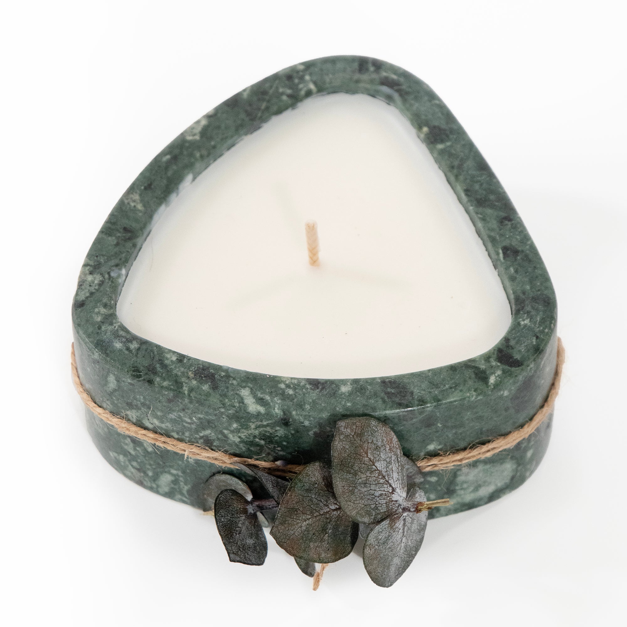 Heart-shaped candle in a green marble holder with twine and leaves on a white background