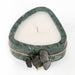 Heart-shaped candle in a green marble holder with twine and leaves on a white background