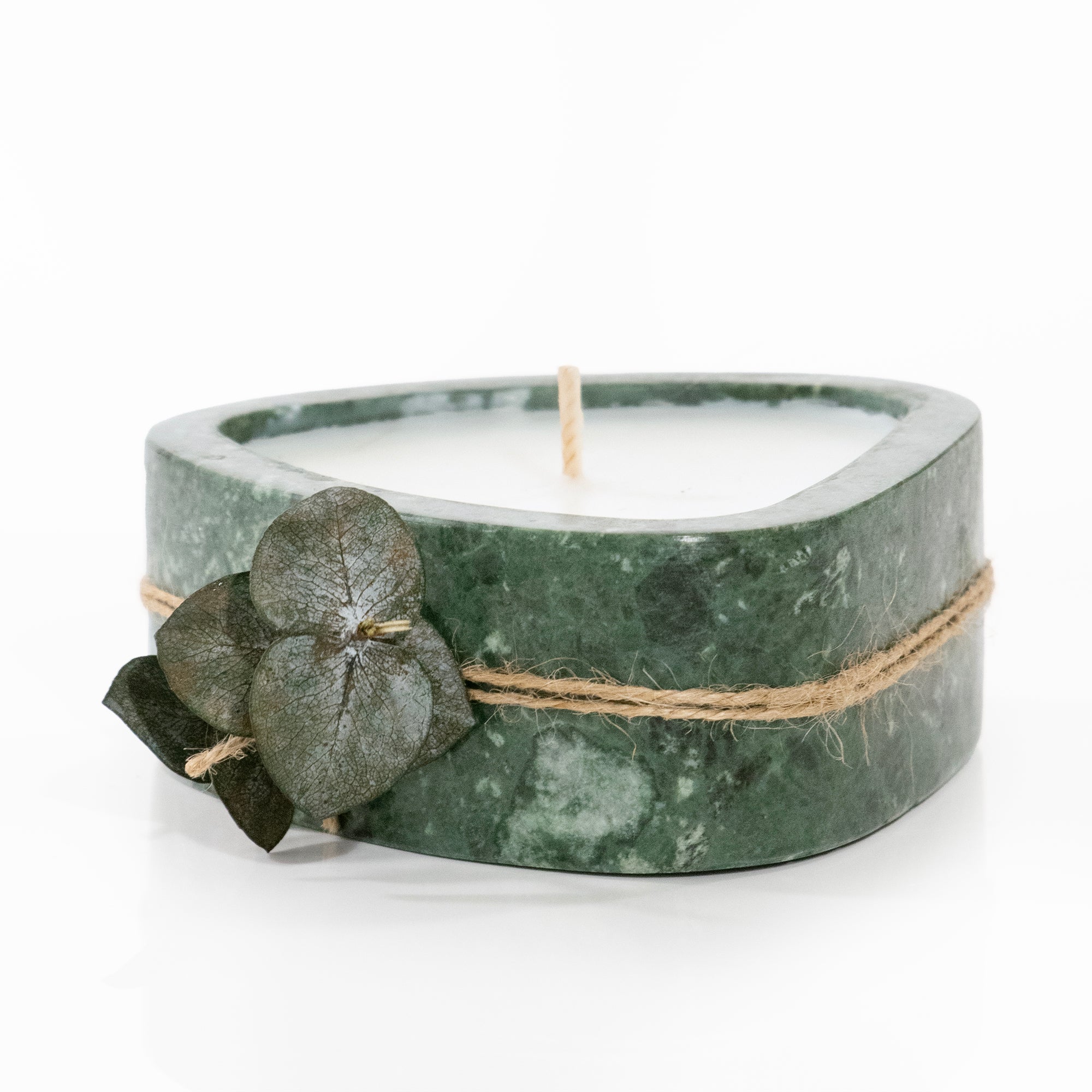 Candle in a green marble container with twine and leaves on a white background