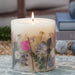 Ivory pillar candle with delicate pressed pink and purple flowers and green leaves decorating the outside of the candle.