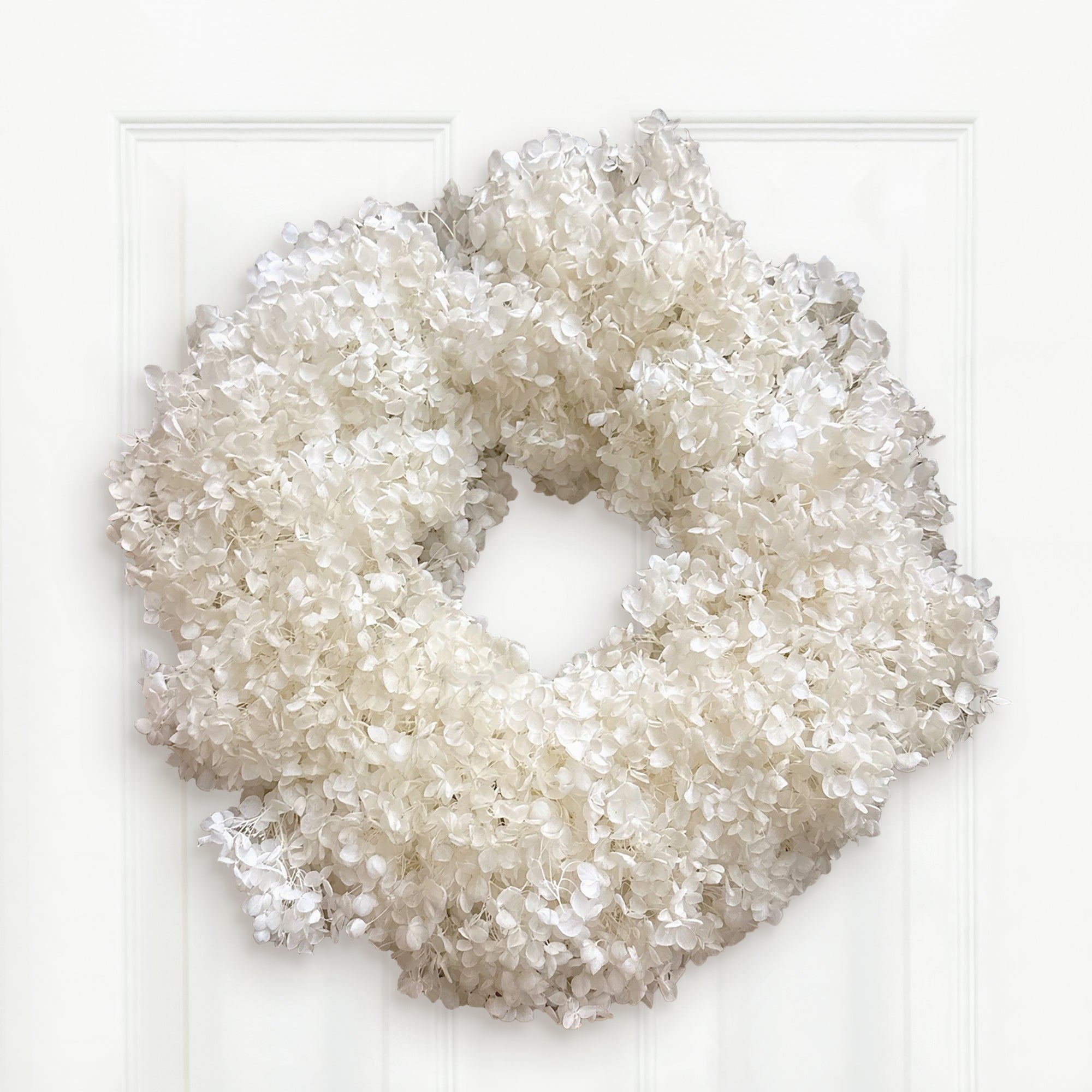 An 18" of Natural White Hydrangea Preserved  Wreath. Hangong on a white door.