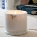 Lit white marble candle cup. Product shot, on a table.