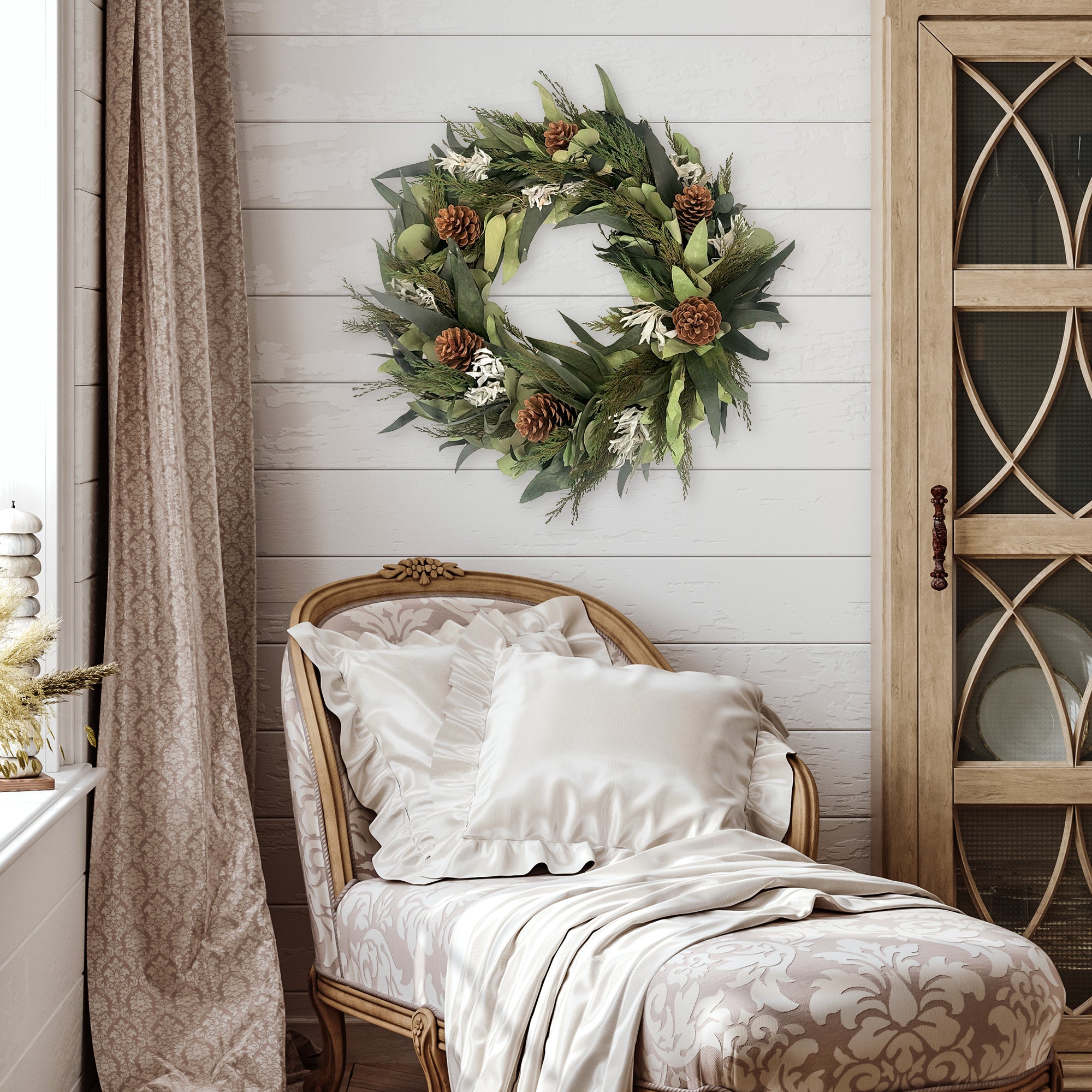 Winter Sage Haoliday wreath hung on a wall above a patterned chair with pillows and a blanket.