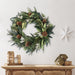 Winter Sage Haoliday wreath hung  on a white wall above a wooden mantel with decorative items.