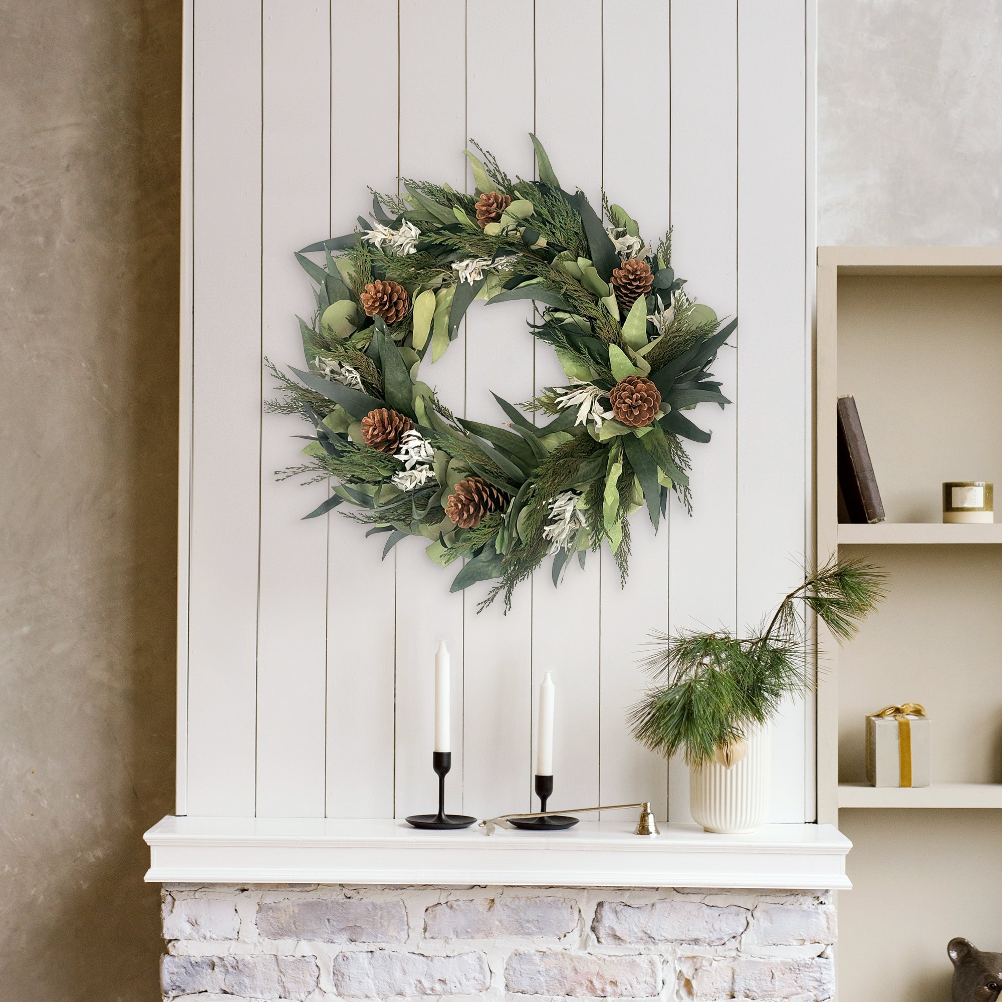 Winter Sage Haoliday wreath hung  on a white wall above a fireplace with candles and decorative items.