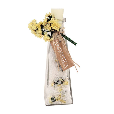 A clear glass perfume bottle with a white wax seal and a cork stopper, decorated with yellow dried flowers, a brown paper tag reading 'ANDALUCIA', and a small green sprig, on a white background.