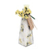 A clear glass bottle with a faceted hexagonal shape, filled with white bath salts and decorated with yellow dried flowers and green leaves. A light brown paper tag tied with a ribbon is attached to the neck, featuring the brand name 'ANDALUCIA'.