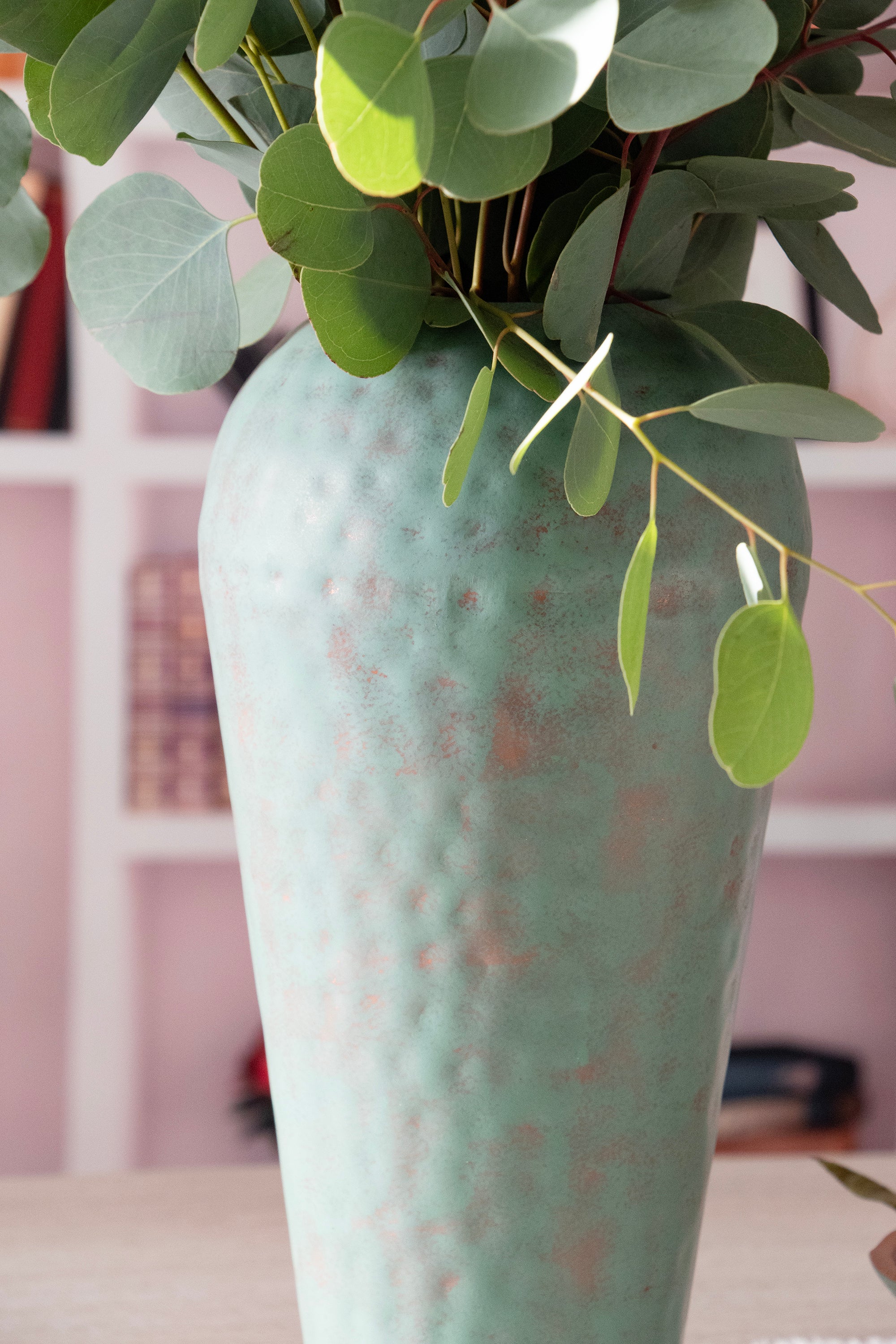 close up of metal vase in room setting with fresh eucalyptus.